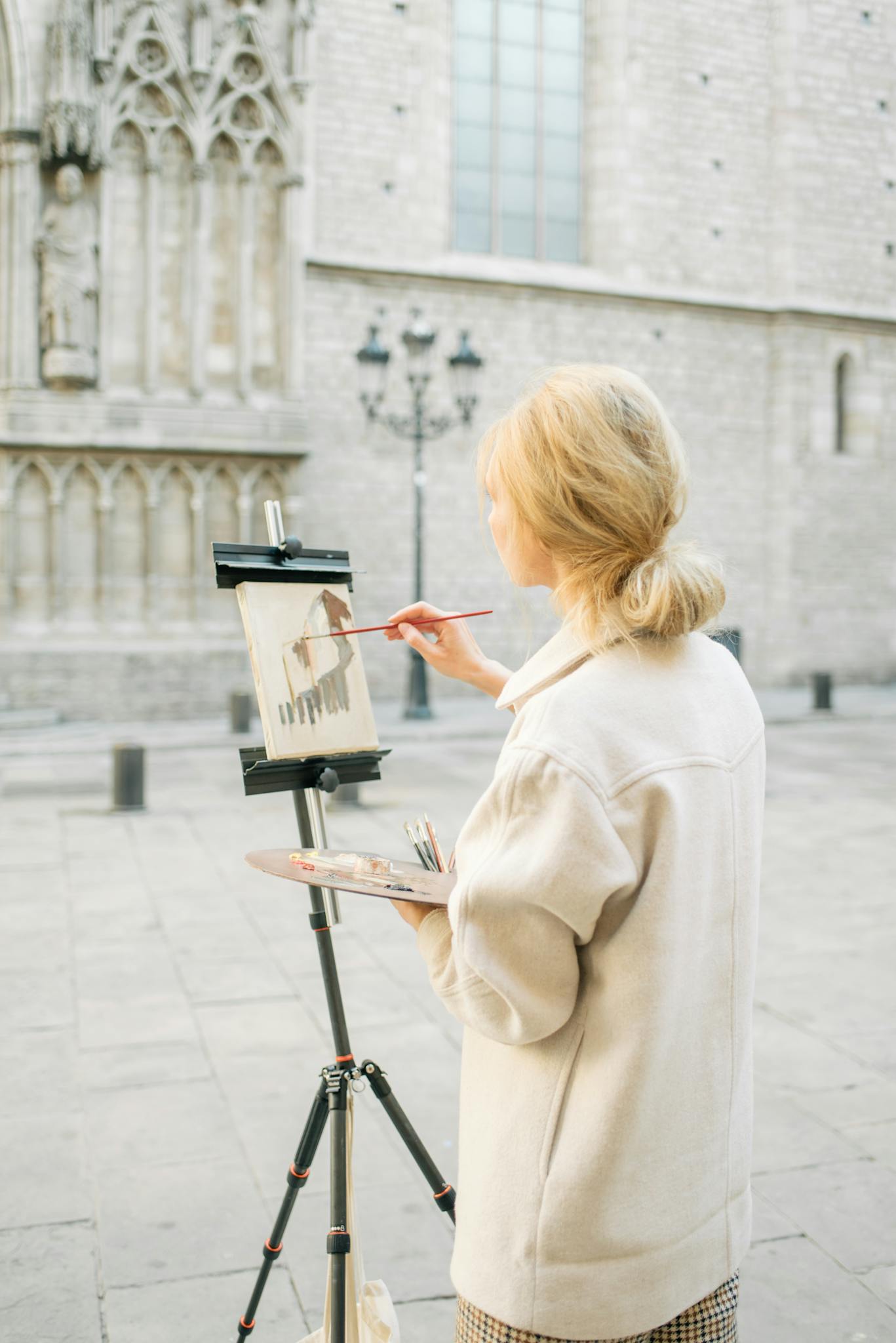 Blonde woman artist painting on canvas outside a historic church in Barcelona street.